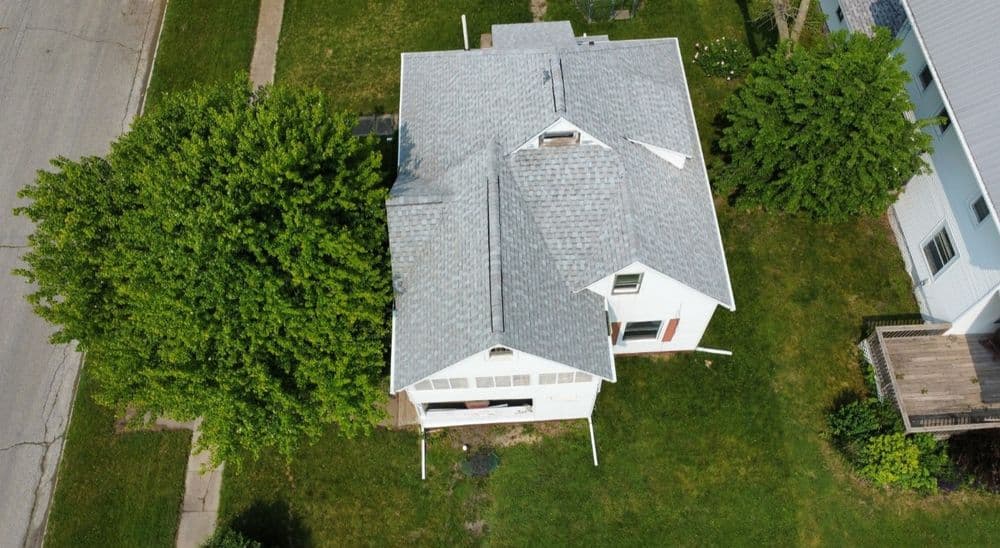 Aerial view of a white house with a gray roof surrounded by green trees and grass.